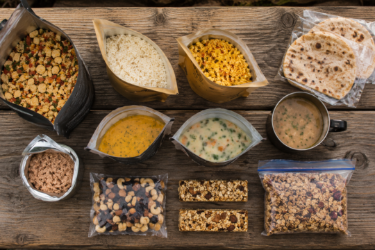 ready to eat camping food flat lay dehydrated meals rice pouches soup packets wraps canned food camping table