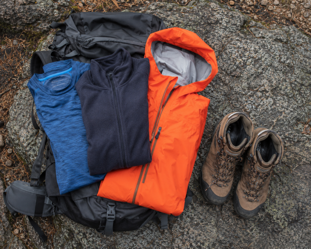 mountain camping for beginners layered clothing system base layer fleece waterproof jacket laid out for high altitude packing