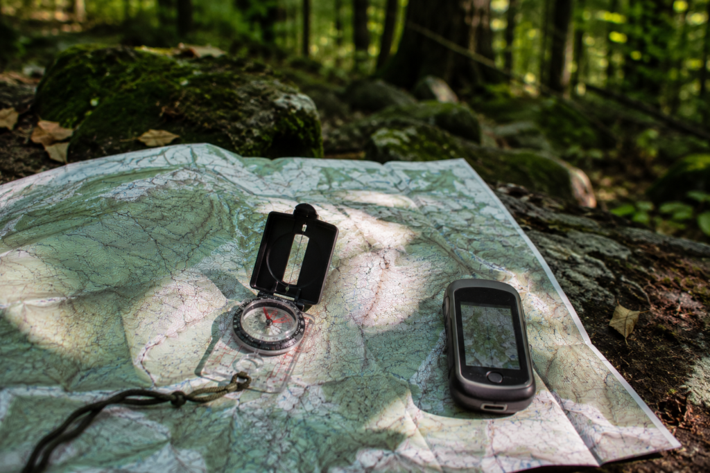 wilderness emergency evacuation navigation tools topographic map compass and GPS device on rock in forest