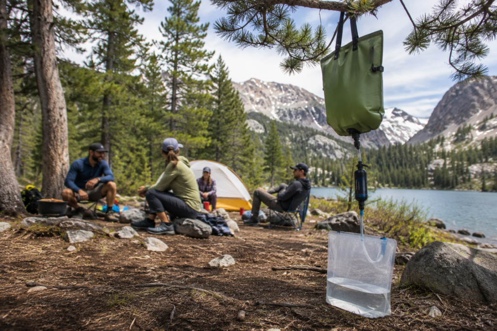 purifying water in the wilderness gravity filter hanging from tree branch campsite group camping several litres