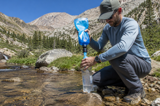 purifying water in the wilderness camper using Sawyer Squeeze filter at mountain stream filling water bottle